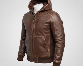 May include: Brown leather hooded jacket with a zip-up front, a front pocket, and ribbed cuffs and hem. The jacket has a hood with a drawstring and a bronze-colored zipper. The jacket is displayed on a white mannequin.