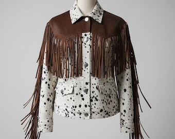 Könnte beinhalten: Weste im Western-Stil mit einem Schulterjoch und Fransen aus braunem Leder. Die Jacke hat ein weißes und schwarzes Fleckenmuster auf dem Körper und den Ärmeln, mit silbernen Knöpfen und zwei Vordertaschen. Der Kragen ist weiß mit schwarzen Punkten.