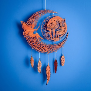 Puede incluir: Adorno de pared de madera con diseño de media luna, silueta de hada y patrones calados intrincados. El diseño incluye un hada sentada en una seta, estrellas y plumas colgantes. El color es marrón cálido sobre un fondo azul.