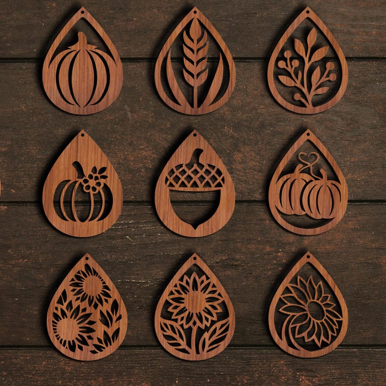 K&ouml;nnte beinhalten: Neun holzfarbene Ohrringe in Tropfenform mit verschiedenen herbstlichen Designs. Die Designs umfassen K&uuml;rbisse, Weizen, Bl&auml;tter und Sonnenblumen. Die Ohrringe sind aus hellbraunem Holz gefertigt und auf einer dunkelbraunen Holzoberfl&auml;che ausgestellt.