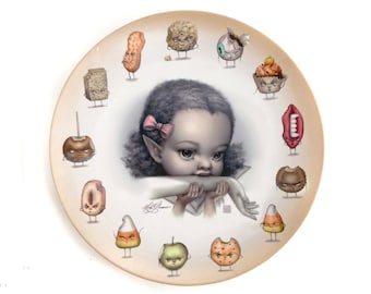 May include: A round ceramic plate featuring a central illustration of a child with pointed ears and a pink hair bow, biting their own arm. The border is decorated with various anthropomorphic food items including candy corn, cookies, and fruit.
