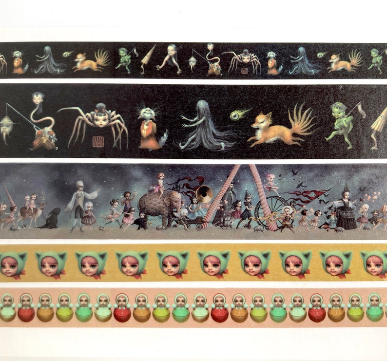 May include: Five strips of washi tape featuring whimsical illustrations of creatures and characters. The first strip features a black background with a spider, a fox, and a green creature. The second strip features a black background with a spider, a fox, and a green creature. The third strip features a dark blue background with a parade of creatures and characters. The fourth strip features a yellow background with a row of green cat faces. The fifth strip features a pink background with a row of green and red nesting dolls.