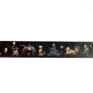 May include: Black and white washi tape with a repeating pattern of various creatures, including a spider, a fox, a ghost, and a fairy. The tape is on a white background.