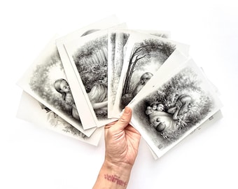 May include: A collection of black and white art prints featuring detailed illustrations of figures in natural settings. The prints showcase scenes of forests, trees, and people, with a focus on shading and intricate details. The word "delirium" is tattooed on the wrist.