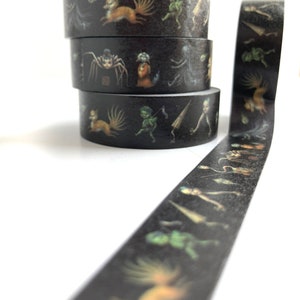 May include: A roll of black washi tape with a repeating pattern of colourful illustrations of fantastical creatures, including a fox, a spider, and a goblin. The tape is wound around three spools.