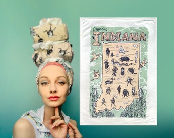 May include: A woman with pink hair is wearing a patterned headscarf. She is holding a tea towel with a map of Indiana and the text "Cryptid Indiana" and "Heart of Hoosier" printed on it. The map is filled with illustrations of various cryptids.