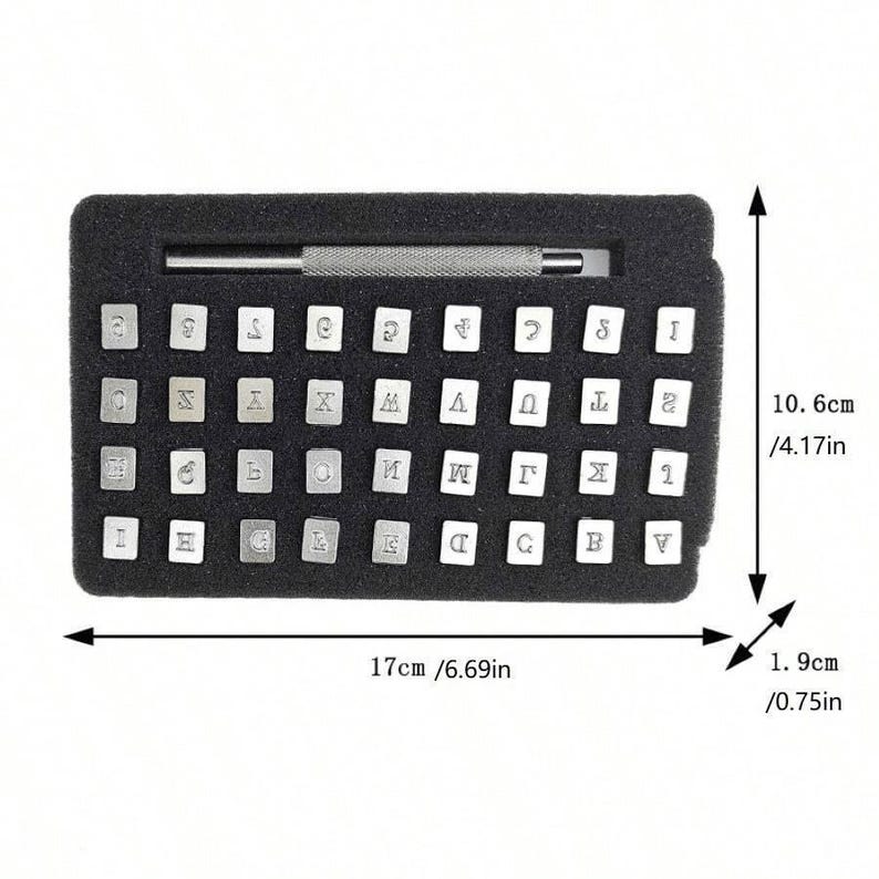 Może przedstawiać: Czarne etui z zestawem 40 metalowych stempli z literami i cyframi. Etui ma 17 cm szerokości i 10,6 cm wysokości. Stempelki są ułożone w rzędach i kolumnach. W zestawie znajduje się metalowe narzędzie do stemplowania.