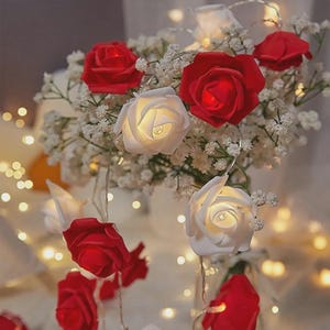 Puede incluir: Cadena de luces LED decorativa con bombillas en forma de rosa roja y blanca. Las rosas se mezclan con pequeñas flores blancas, creando un ambiente romántico. Ideal para la decoración del hogar o eventos especiales. Funciona con pilas.