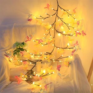 K&ouml;nnte beinhalten: Eine Lichterkette mit zarten, bunten Schmetterlings-Dekorationen. Die Lichter sind an einem astf&ouml;rmigen Draht befestigt und erzeugen ein warmes, einladendes Licht.