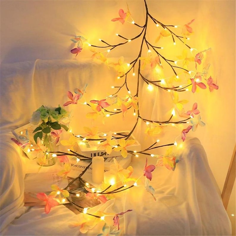 K&ouml;nnte beinhalten: Eine Lichterkette mit zarten, bunten Schmetterlings-Dekorationen. Die Lichter sind an einem astf&ouml;rmigen Draht befestigt und erzeugen ein warmes, einladendes Licht.