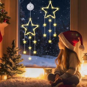 Puede incluir: Una escena festiva con luces de cadena en forma de estrella colgando frente a una ventana con un fondo nevado. Un niño con un gorro de Papá Noel rojo está sentado cerca. Las luces y la decoración crean un ambiente cálido y acogedor.