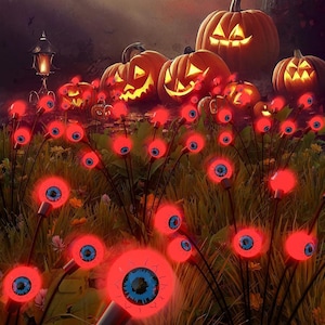 Puede incluir: Una escena de Halloween con calabazas naranjas brillantes con caras talladas y decoraciones rojas iluminadas en forma de ojo en un campo cubierto de hierba. Una farola de estilo vintage es visible en el fondo, con una atmósfera oscura y espeluznante.