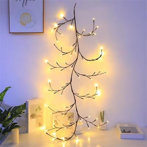 K&ouml;nnte beinhalten: Eine Lichterkette mit warmwei&szlig;en Lichtern in Form von Zweigen mit kleinen Gl&uuml;hbirnen. Die Lichter sind in einem langen, kaskadierenden Design zusammengef&uuml;gt, perfekt, um jedem Raum eine stimmungsvolle Atmosph&auml;re zu verleihen.