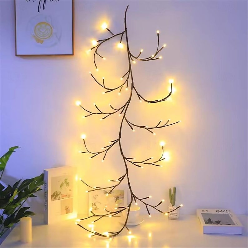 K&ouml;nnte beinhalten: Eine Lichterkette mit warmwei&szlig;en Lichtern in Form von Zweigen mit kleinen Gl&uuml;hbirnen. Die Lichter sind in einem langen, kaskadierenden Design zusammengef&uuml;gt, perfekt, um jedem Raum eine stimmungsvolle Atmosph&auml;re zu verleihen.
