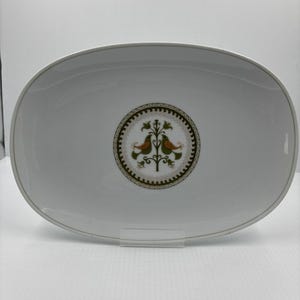 May include: Oval white serving platter with a gold rim. The center features a circular design with two orange birds perched on a green tree. The design is surrounded by a decorative border.