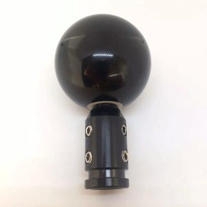 May include: Black gear shift knob with a round, smooth, black ball on top and a black metal base with four silver screws.