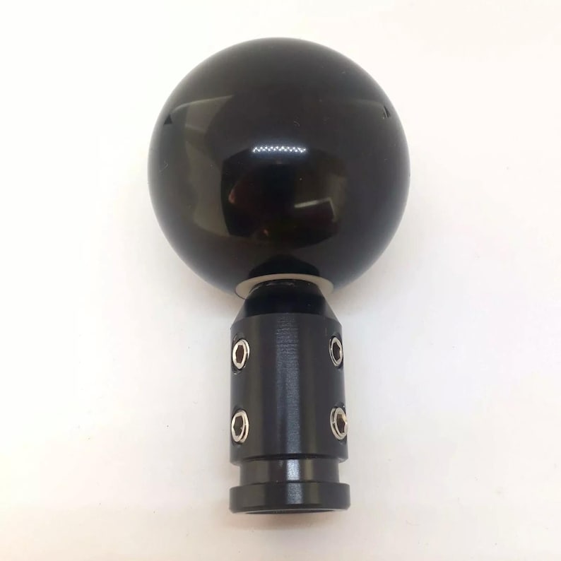 May include: Black gear shift knob with a round, smooth, black ball on top and a black metal base with four silver screws.