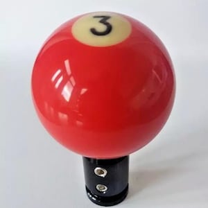 May include: Red billiard ball with a white number 3 on it. The ball is attached to a black gear shift knob.