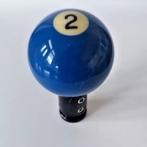 May include: Blue billiard ball with a white number 2 on it. The ball is attached to a black gear shift knob.
