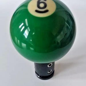 May include: Green billiard ball with a white number six on it. The ball is attached to a black gear shift knob.