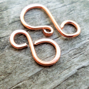 May include: Two copper-coloured metal wire loops, each with a single loop, are shown on a wooden surface. The loops are connected to each other.