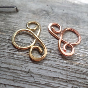 May include: Two wire loops, one gold and one copper, are shaped into a figure eight design. The loops are on a wooden surface.