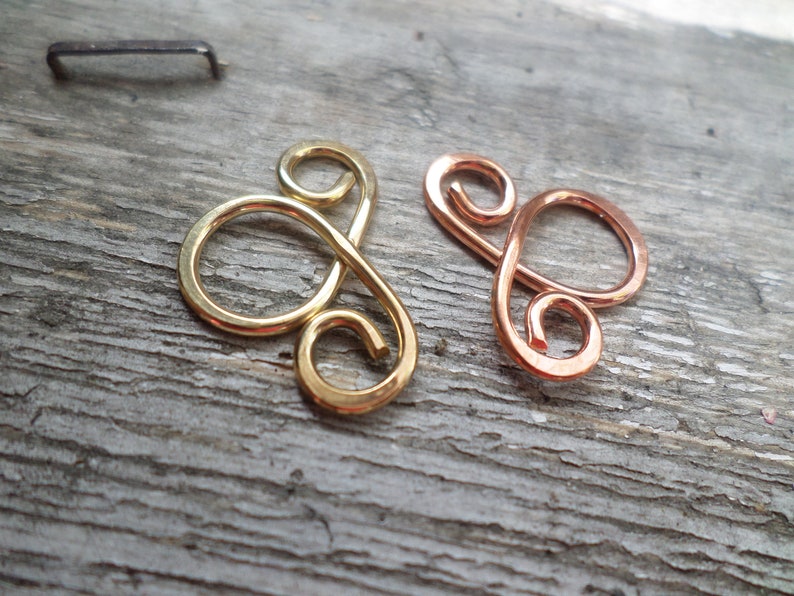 May include: Two wire loops, one gold and one copper, are shaped into a figure eight design. The loops are on a wooden surface.