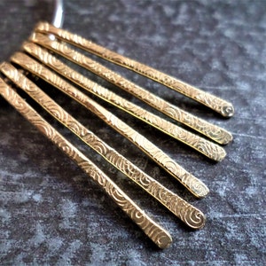 May include: Gold pendant necklace with a fan-shaped design of seven thin, textured bars. Each bar has a swirling pattern.