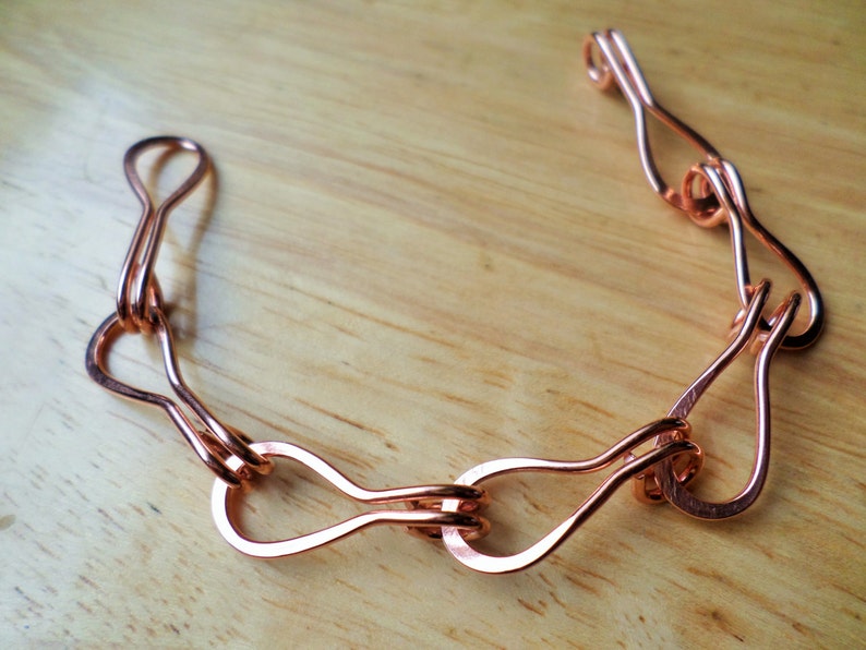 Puede incluir: Un collar de cadena de metal de color cobre con m&uacute;ltiples bucles entrelazados. La cadena est&aacute; hecha de un solo alambre que se dobla y se tuerce en una serie de bucles.