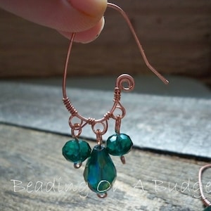 Peut inclure: Boucles d'oreilles en fil de cuivre avec un cristal vert en forme de larme et deux plus petits cristaux verts ronds suspendus au bas.