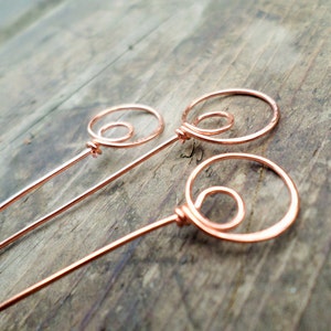 May include: Three copper wire circles with a smaller circle inside each larger circle. The circles are attached to long copper wire stems.