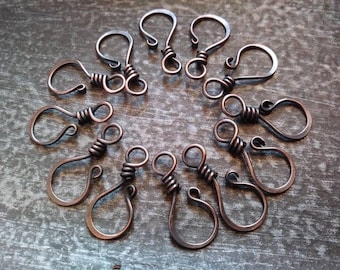 May include: A close-up of a group of 12 copper-colored metal clasps. The clasps are in the shape of a hook with a twisted wire design.