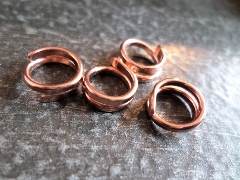 K&ouml;nnte beinhalten: Vier Kupferringe, jeder mit einem doppelschichtigen Design, sind auf einer strukturierten Oberfl&auml;che angeordnet. Die Ringe sind alle gleich gro&szlig; und gleich geformt und aus gl&auml;nzendem, metallischem Kupfer gefertigt.