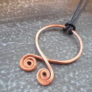 May include: A copper wire pendant necklace with a double spiral design. The necklace is on a black leather cord.