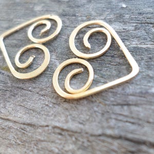 May include: Gold-toned metal earrings with a geometric design. The earrings are shaped like a diamond with three spiral shapes inside.