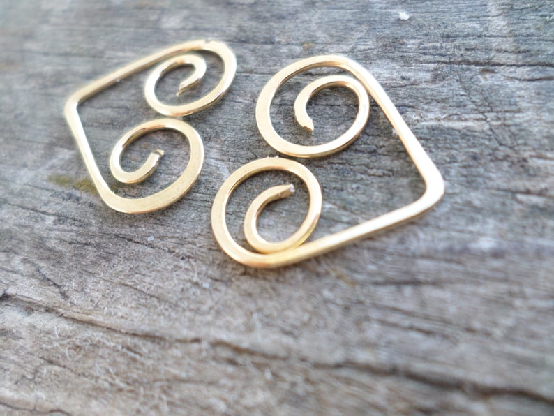 May include: Gold-toned metal earrings with a geometric design. The earrings are shaped like a diamond with three spiral shapes inside.