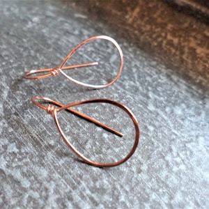 May include: A pair of rose gold teardrop shaped earrings made from wire.