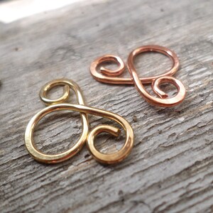 May include: Two wire-wrapped infinity symbols, one gold and one copper, on a wooden surface.