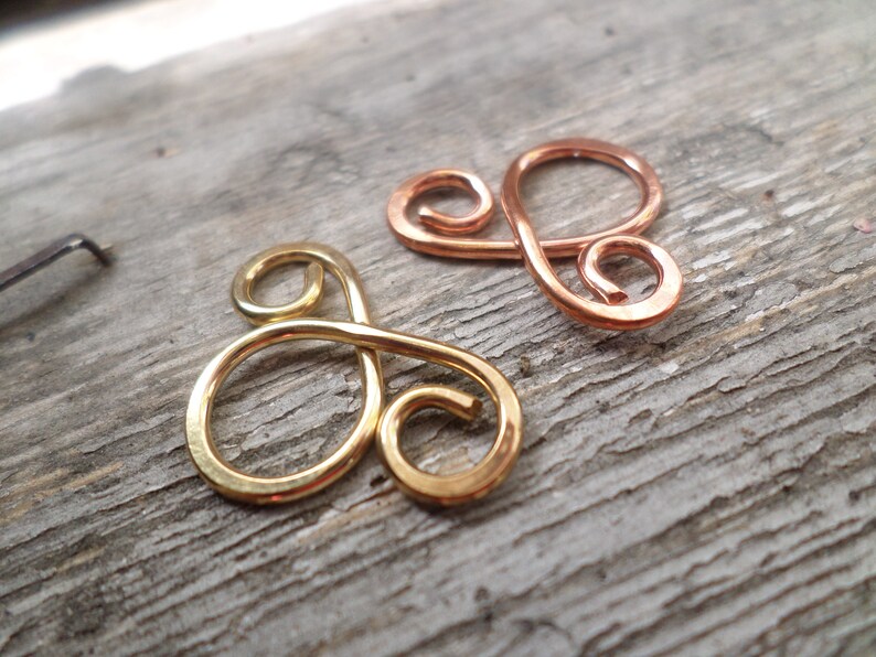 May include: Two wire-wrapped infinity symbols, one gold and one copper, on a wooden surface.