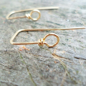 May include: A pair of gold-toned earrings with a simple, minimalist design. Each earring features a small, circular loop at the end of a thin, straight wire.