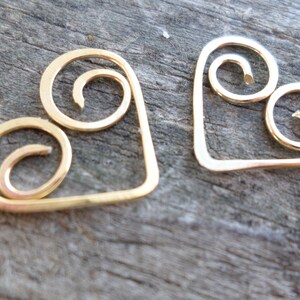 May include: Two gold-colored metal heart-shaped charms with a swirl design.