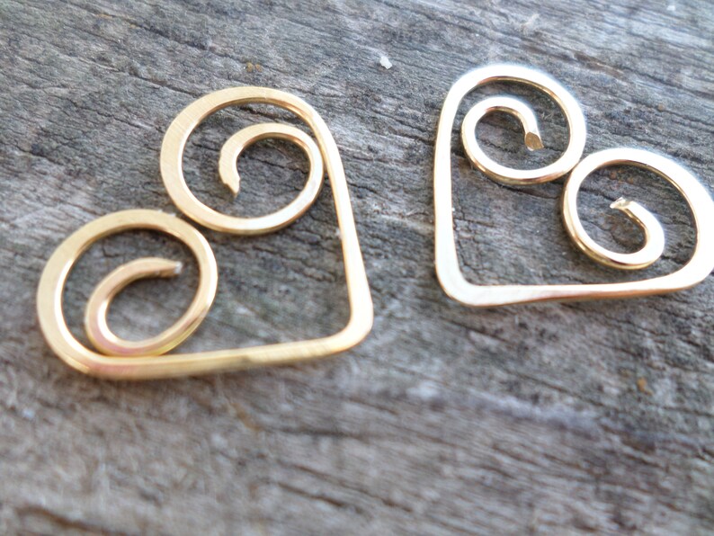 May include: Two gold-colored metal heart-shaped charms with a swirl design.