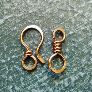 May include: Two copper-colored clasps for jewelry making. One clasp is a hook and loop style, the other is a simple loop.
