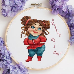 May include: A cross-stitch embroidery hoop featuring a cartoon woman with brown hair, blue eyes, and a red outfit. The text "Perfect as I am!" is written in red. Purple flowers surround the hoop.