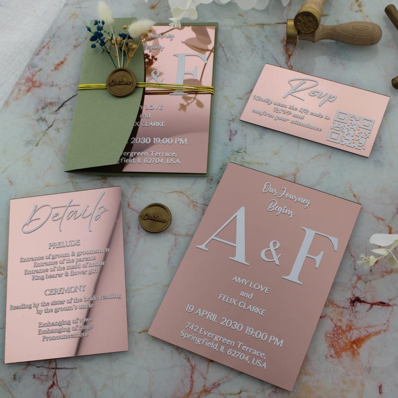 May include: Rose gold wedding invitation suite with white calligraphy. The invitation includes details about the ceremony, reception, and RSVP information. The invitation is decorated with a wax seal and greenery.