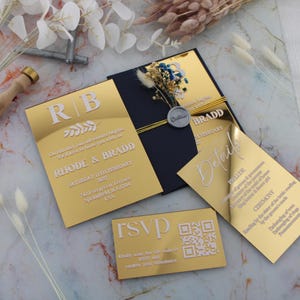 May include: Gold mirror acrylic wedding invitations with white text. The invitations feature the couple's names, wedding date, and location. The RSVP card includes a QR code for guests to confirm their attendance.
