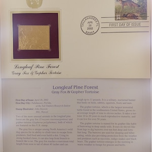 Puede incluir: Un sello de primer día de emisión con un zorro gris y una tortuga gopher. El sello es dorado y tiene el texto "Longleaf Pine Forest Gray Fox & Gopher Tortoise" impreso en él. El sello está rodeado por un borde rojo.