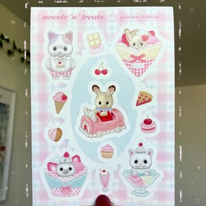 Peut inclure: Une planche d'autocollants avec des illustrations d'animaux et de desserts. Les autocollants représentent un chat dans une coupe glacée, un lapin dans une voiture et un ours avec un gâteau. Le texte "sweets 'n' treats" et "gracie's critters" sont visibles.