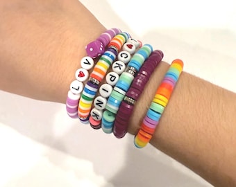May include: A stack of colorful beaded bracelets with letter beads spelling out "PINK" and "LOVE". The bracelets are on a person's wrist.