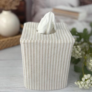 Peut inclure: Une housse de bo&icirc;te &agrave; mouchoirs carr&eacute;e pr&eacute;sentant un motif &agrave; rayures verticales beige clair et blanc. La housse en tissu est con&ccedil;ue pour recouvrir une bo&icirc;te &agrave; mouchoirs standard, avec une ouverture centrale au sommet pour un mouchoir blanc.